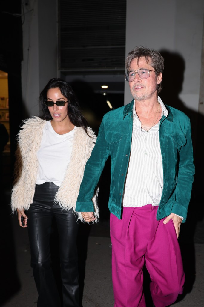 Brad Pitt in a teal jacket and magenta trousers walking with Ines de Ramon after a concert in Paris