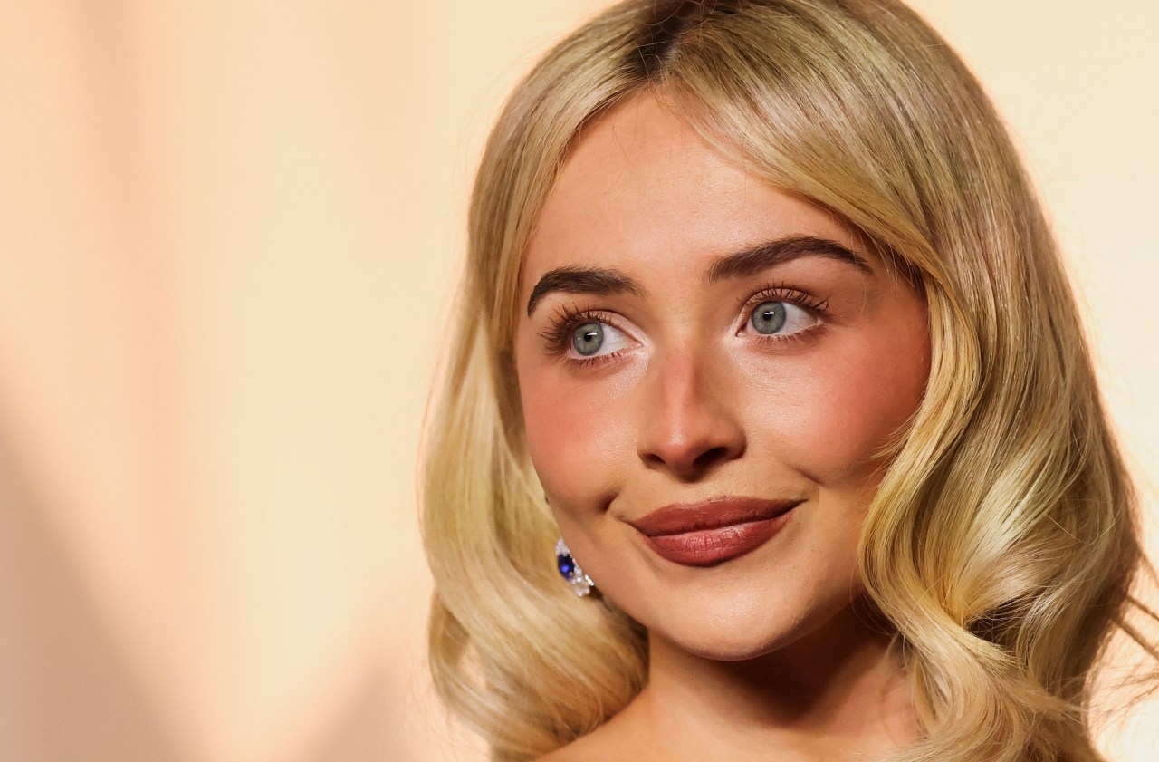 Close-up of Sabrina Carpenter with blonde wavy hair and blue sapphire drop earrings, smiling slightly at the Academy Museum Gala.