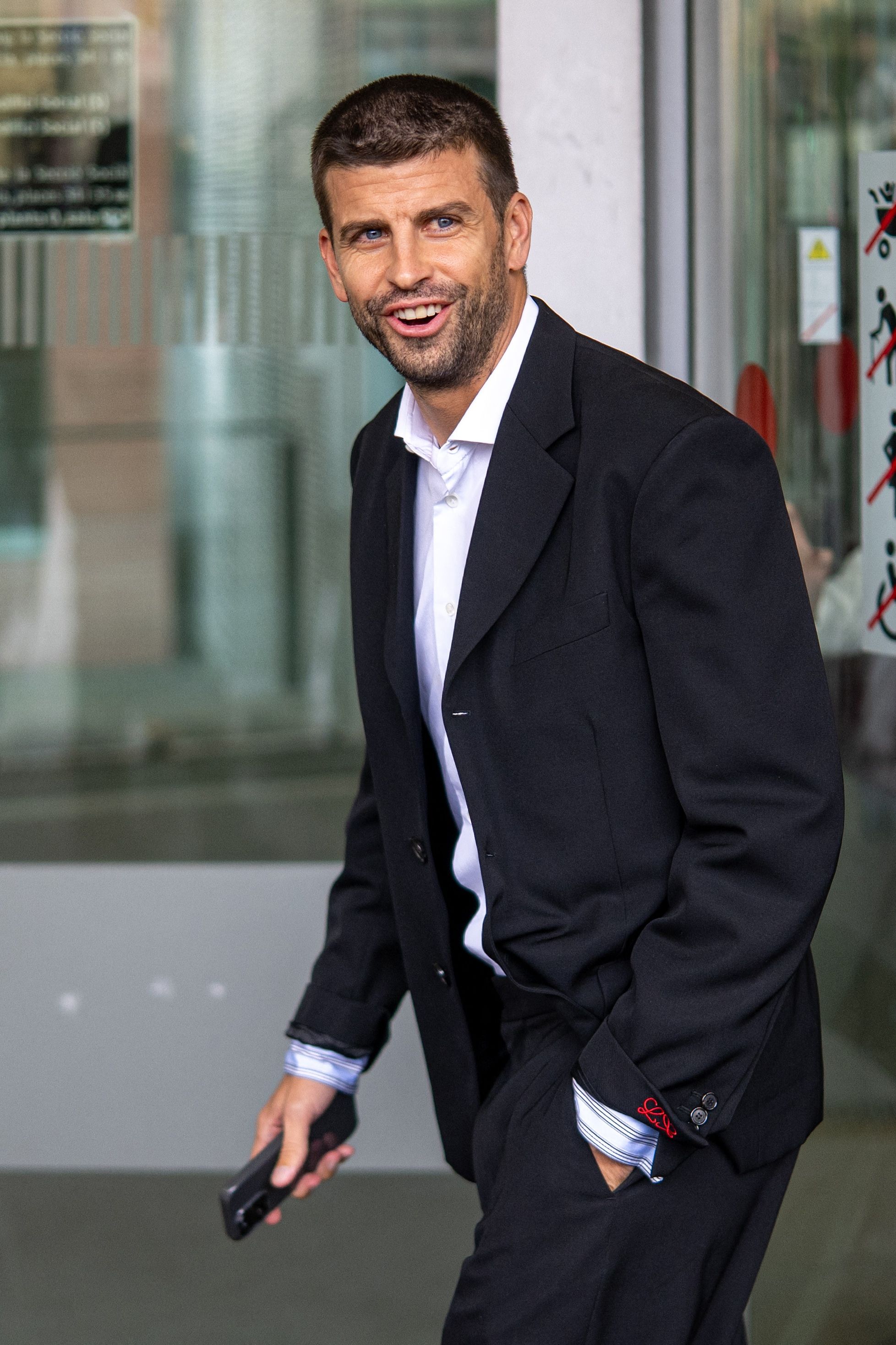 Man in a dark blazer and white shirt smiling and holding a phone outside a courthouse.